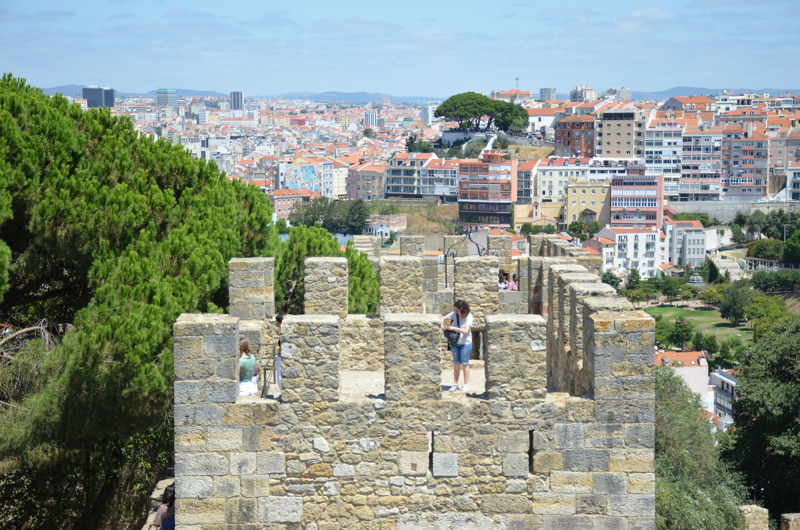 A stone battlement tower at Castelo de São Jorge in Lisbon, with visitors looking out over the city's rooftops and distant hills